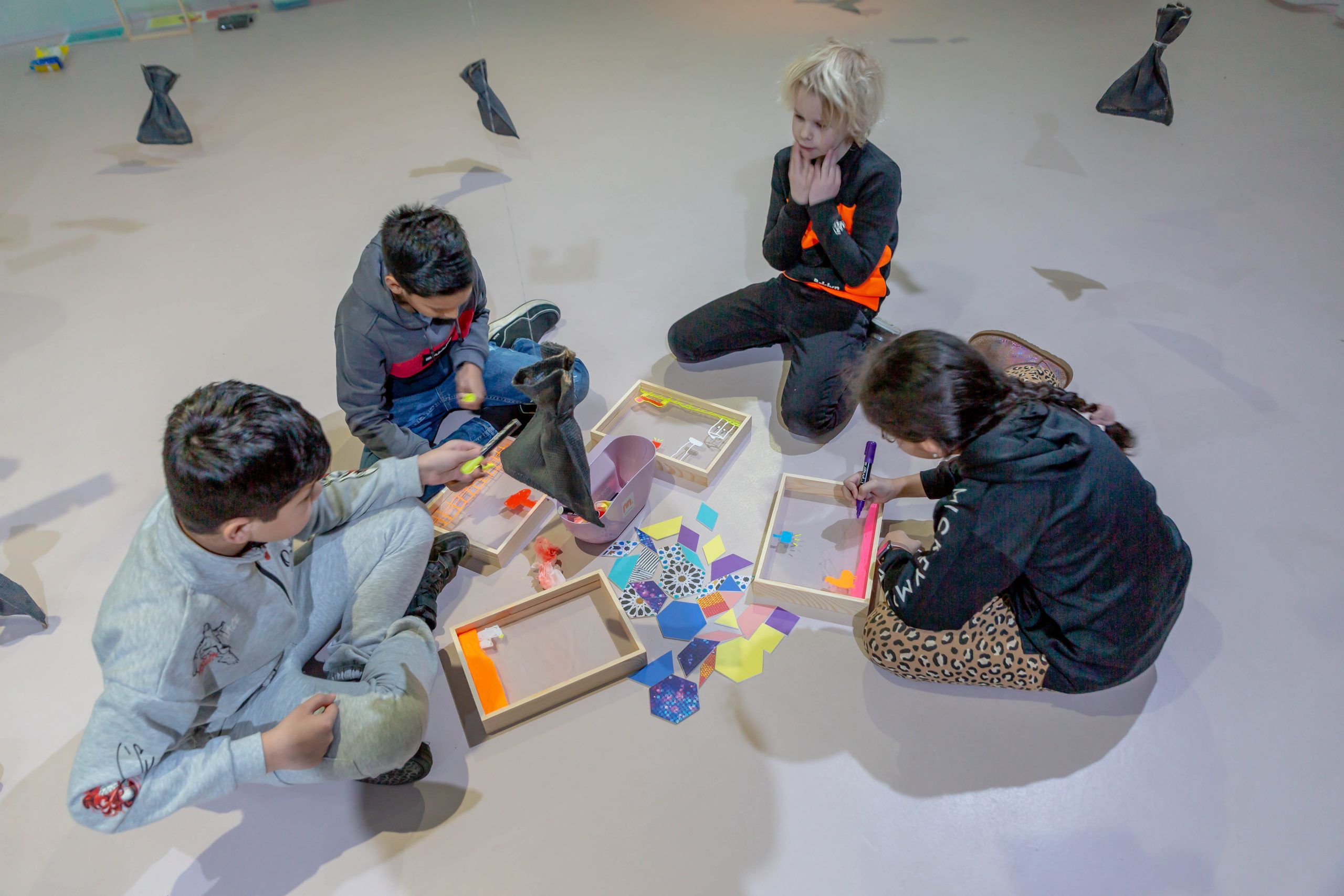 Vier kinderen zitten op de grond, aan het werk met hun eigen mini-installatie.